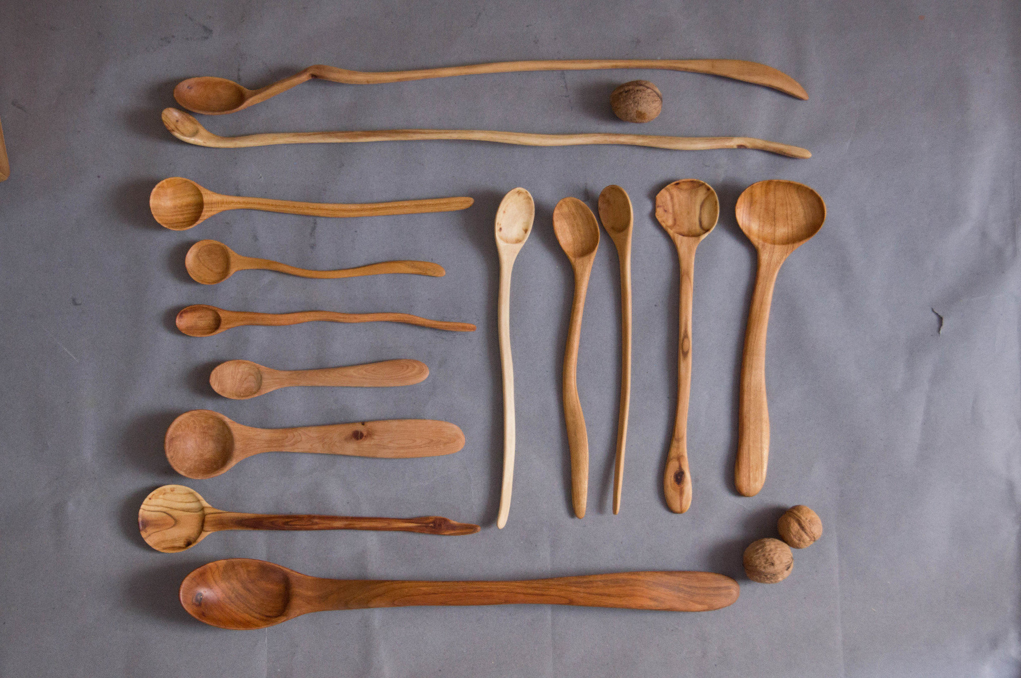 Handcrafted wooden spoons and walnuts on gray background.