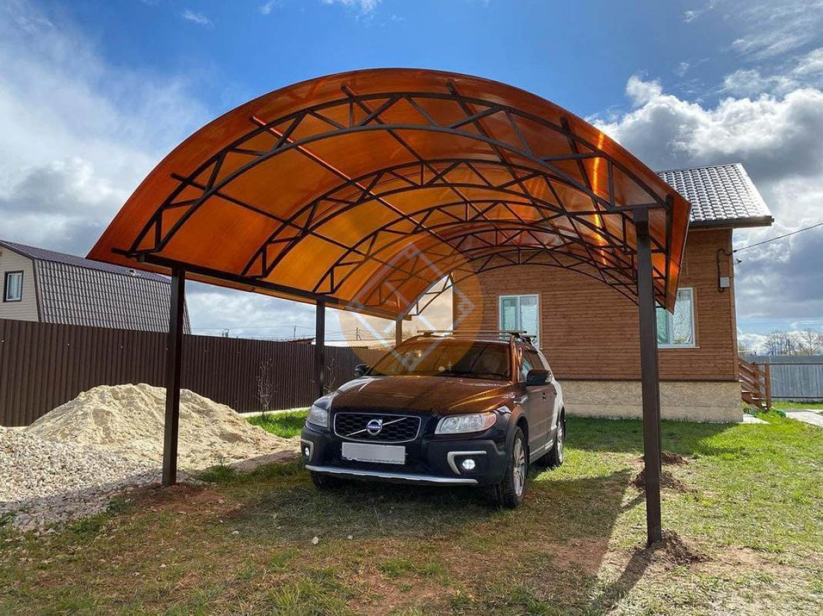 A black Volvo SUV is parked under a curved metal and polycarbonate carport next to a brown house on a grassy yard.