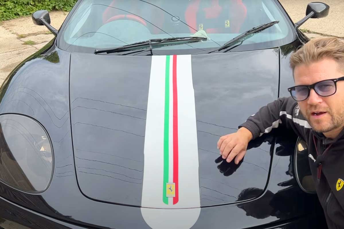 A sleek black Ferrari with a racing stripe in Italian colors, parked on a driveway, as someone leans on its hood.