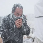 A man standing in the snow looking at his cell phone