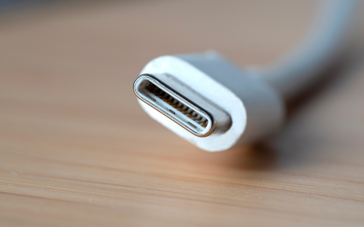 Close-up of a USB-C connector against a wooden background, highlighting its sleek, oval shape and metallic edge.