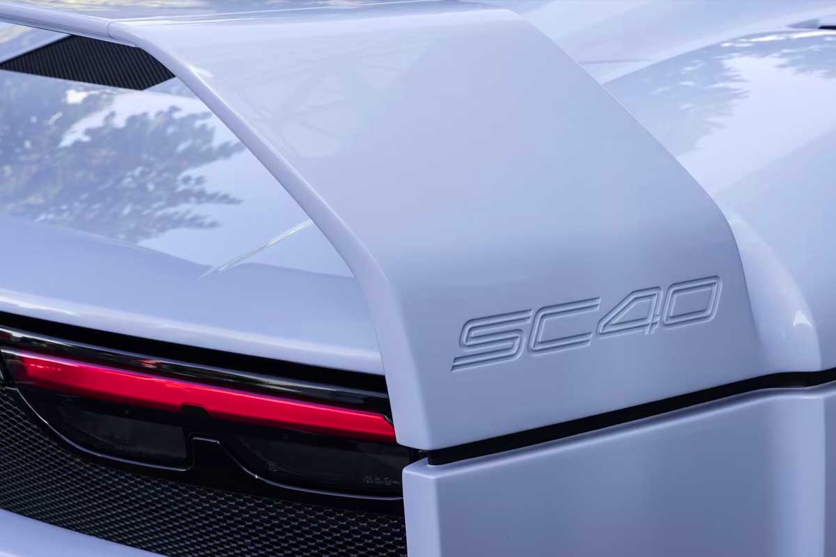 Close-up of a sleek car's rear featuring a prominent SC40 badge and an aerodynamic spoiler against a soft gray background.